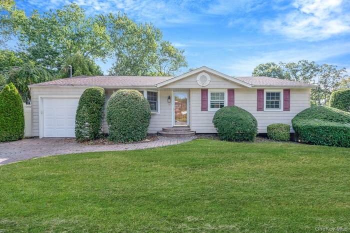 Single story home with an attached garage, roof with shingles, a front yard, and driveway