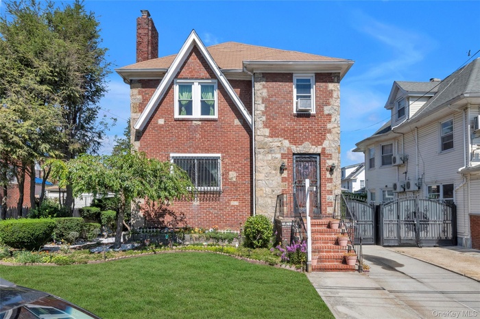Tudor-style house with brick siding, a gate, a front lawn, a chimney, and roof with shingles