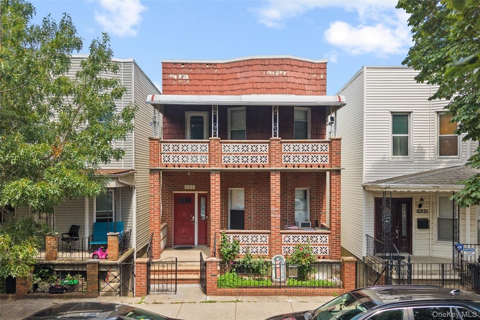 View of front of property featuring a fenced front yard, a porch, a gate, brick siding, and mansard roof