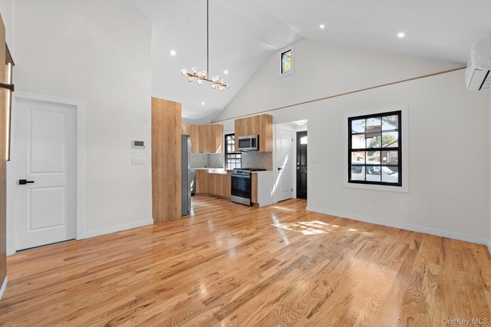 Unfurnished living room featuring high vaulted ceiling, a chandelier, light wood-style floors, a wall mounted air conditioner, and recessed lighting
