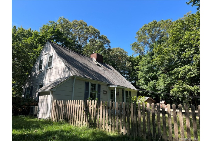 View of side of home featuring a shingled roof, a chimney, and view of wooded area