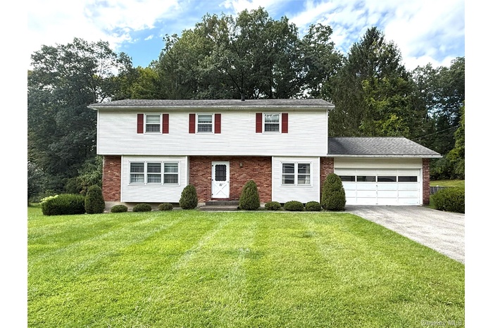 Colonial home featuring concrete driveway, a front yard, an attached garage, and brick siding