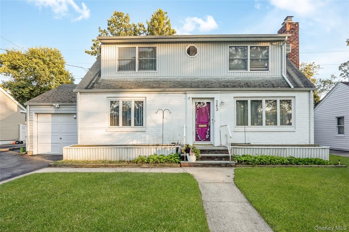 View of front of property with a front yard, a chimney, asphalt driveway, brick siding, and a garage