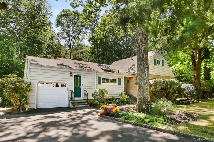 View of front of house with a chimney, view of scattered trees, asphalt driveway, and an attached garage