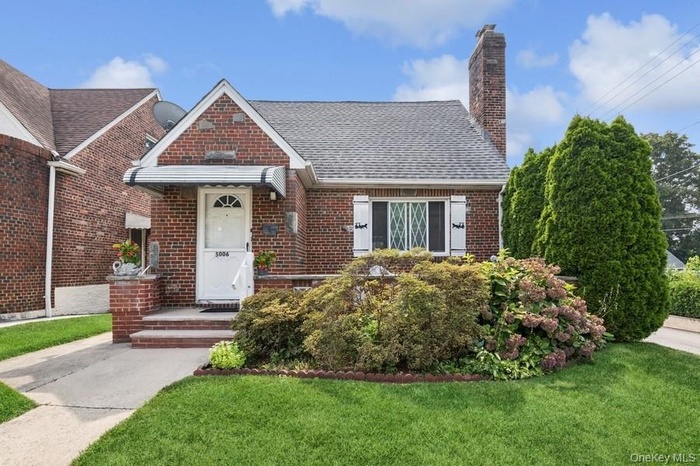 View of front of home with brick siding, a front yard, a chimney, and roof with shingles