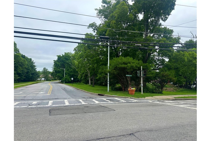 View of asphalt road with street lighting, view of wooded area, and curbs