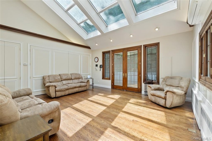 Living area with light wood-style flooring, a skylight, high vaulted ceiling, radiator, and recessed lighting