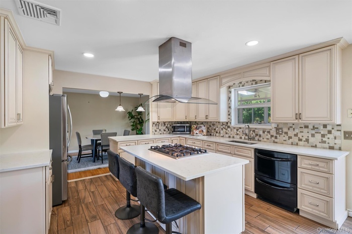 Kitchen featuring island range hood, appliances with stainless steel finishes, a sink, a kitchen breakfast bar, and light countertops