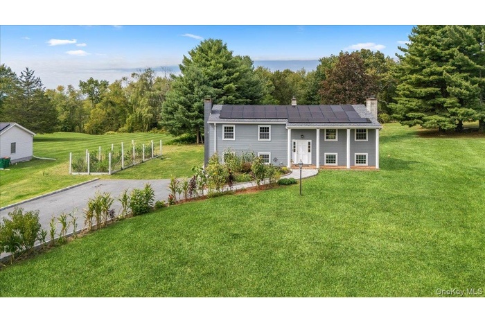 View of front of home with a chimney, a front lawn, and roof mounted solar panels