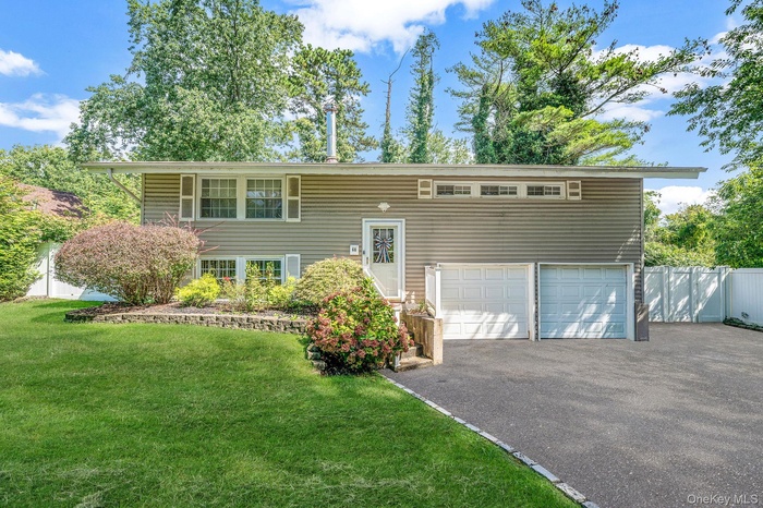 Split foyer home with driveway, an attached garage, and a front lawn
