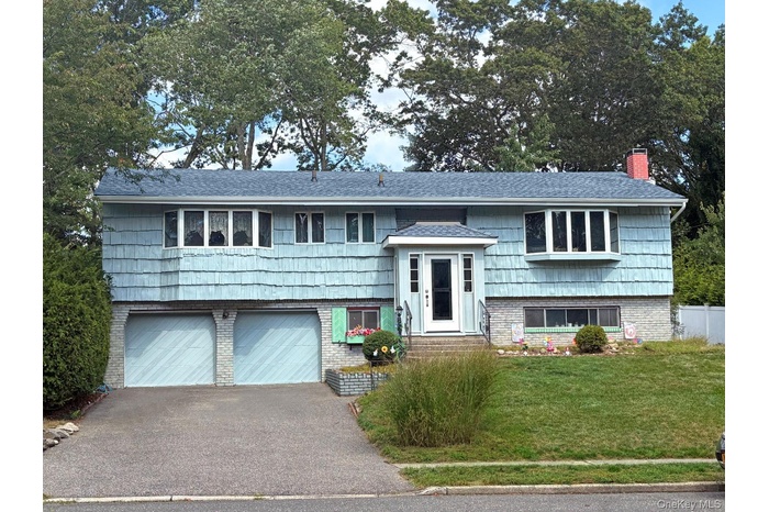 Split foyer home with driveway, brick siding, an attached garage, a chimney, and a front yard
