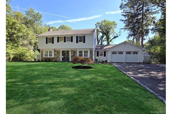 Colonial-style house with asphalt driveway, a front yard, a chimney, stone siding, and an attached garage