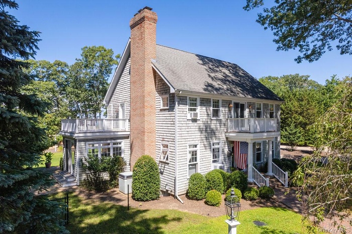 Back of property featuring roof with shingles, a chimney, a balcony, and a lawn