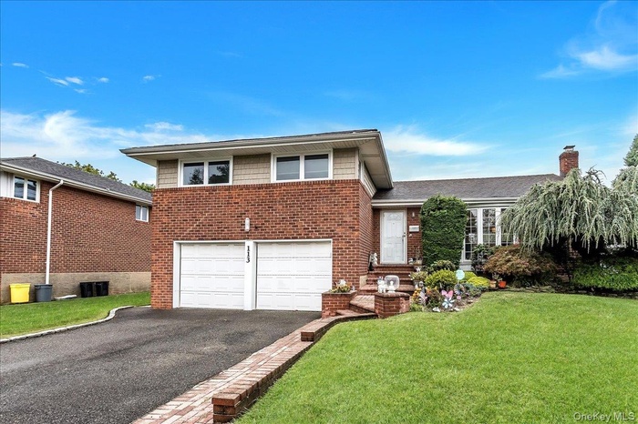 Tri-level home featuring asphalt driveway, a front lawn, a garage, brick siding, and a chimney