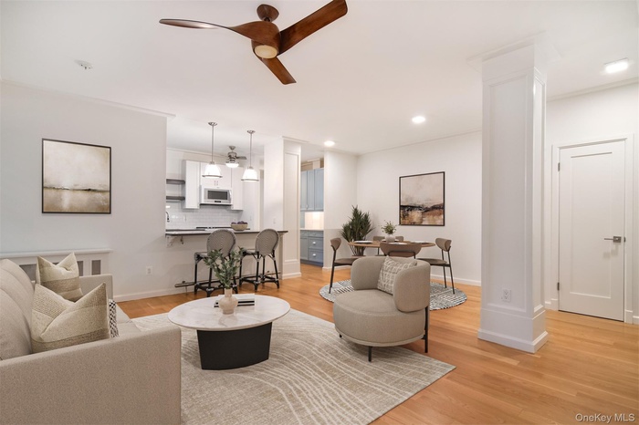 Living room with light wood-type flooring, a ceiling fan, decorative columns, and recessed lighting