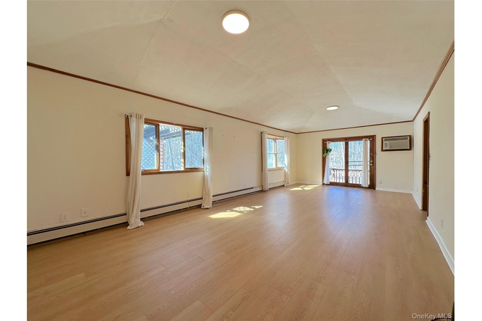 Unfurnished room with baseboards, a wall unit AC, light wood-style flooring, vaulted ceiling, and crown molding