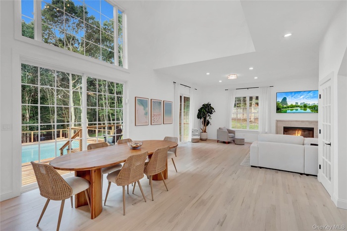 Dining area featuring a glass covered fireplace, light wood-style flooring, recessed lighting, and a high ceiling