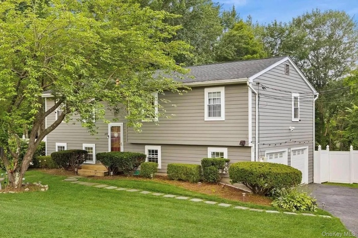 Raised ranch with an attached garage, a front yard, driveway, and a shingled roof