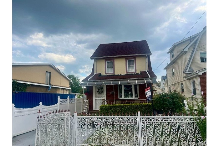 Colonial inspired home with covered porch, a fenced front yard, a gate, and roof with shingles