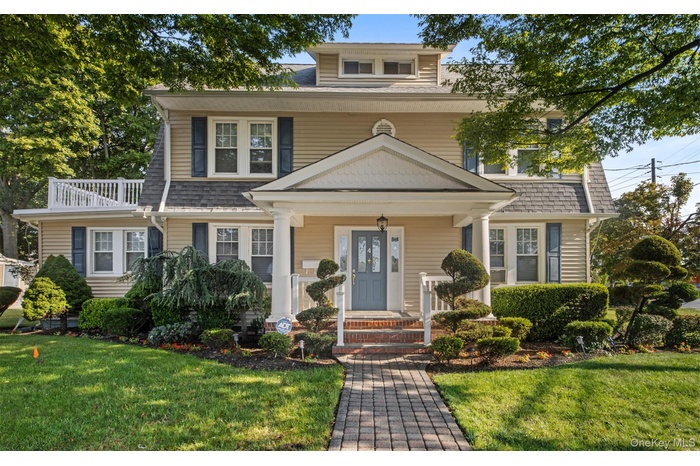View of front of home with covered porch, a front yard, and a shingled roof