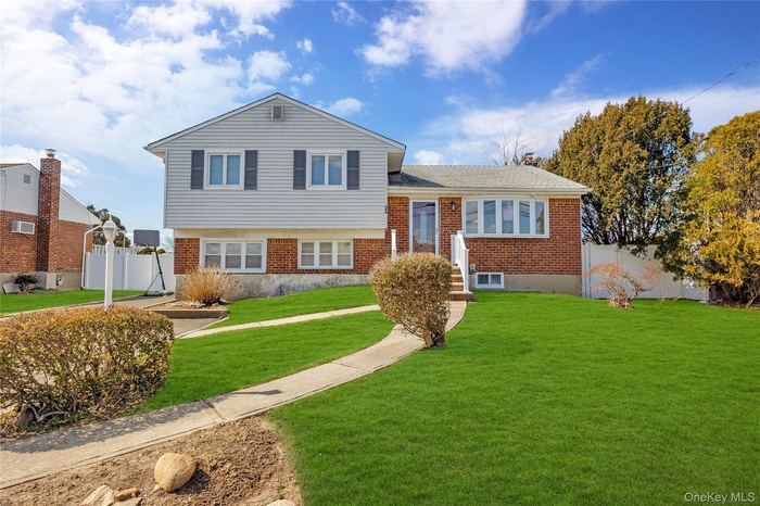 Tri-level home with a front lawn, fence, and brick siding