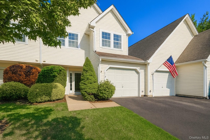 View of front facade with a garage, driveway, roof with shingles, and a front yard
