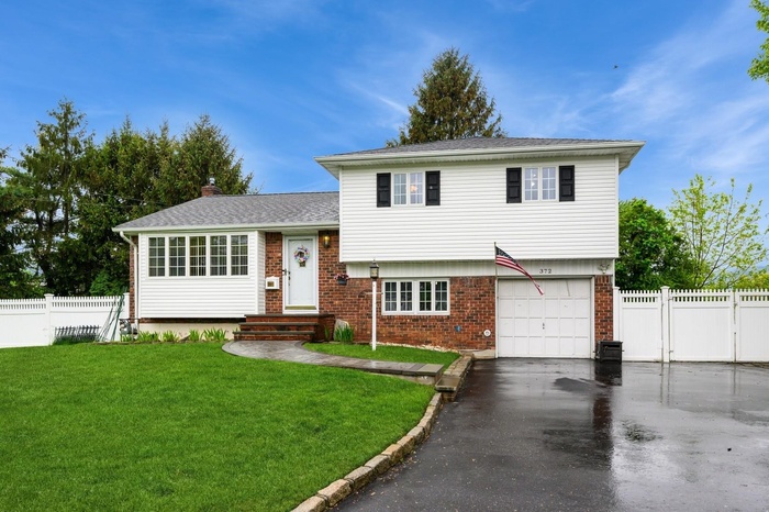 Split level home featuring brick siding, driveway, an attached garage, a chimney, and roof with shingles