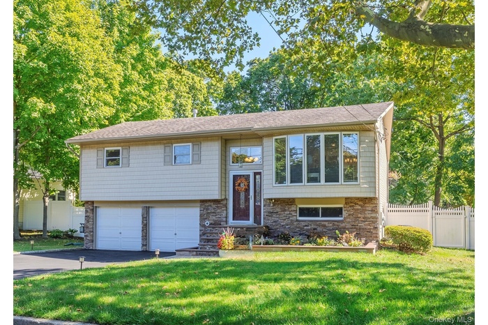 Raised ranch featuring stone siding, driveway, and a garage