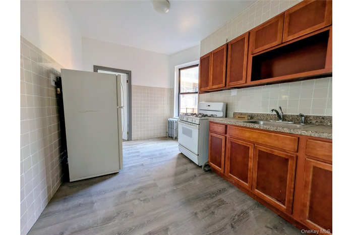 Kitchen featuring white appliances, tile walls, light wood-style flooring, radiator heating unit, and brown cabinets