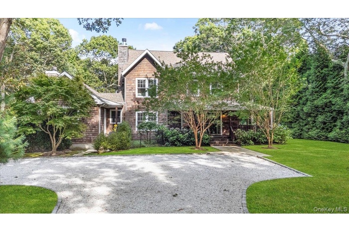 View of front of house featuring a front yard, a chimney, a shingled roof, covered porch, and view of scattered trees