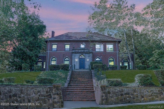 Colonial home with a front lawn, stairway, and brick siding