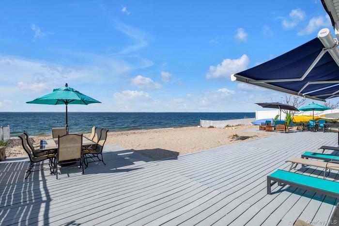Wooden terrace with outdoor dining space and view of water and beach