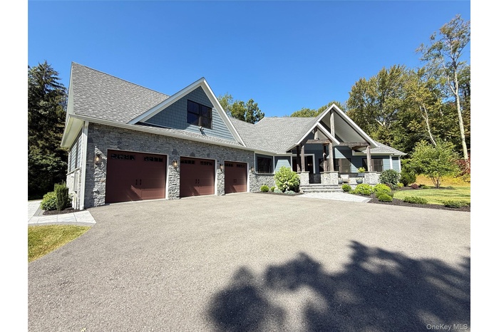 Craftsman-style home featuring stone siding, driveway, an attached garage, roof with shingles, and a porch