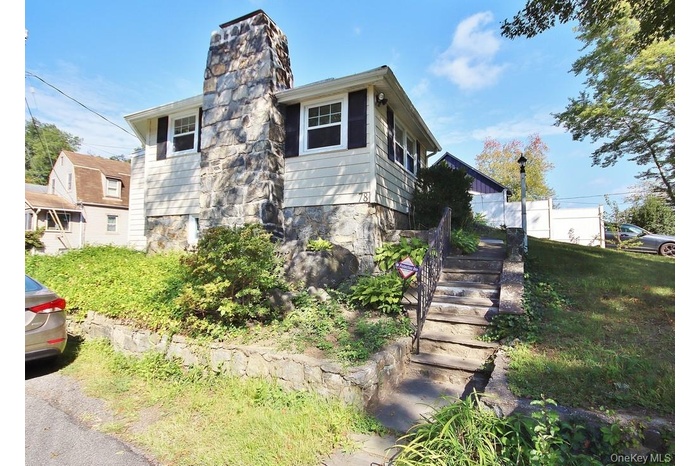 View of front facade featuring stone fireplace siding, a chimney, and main entry stairway