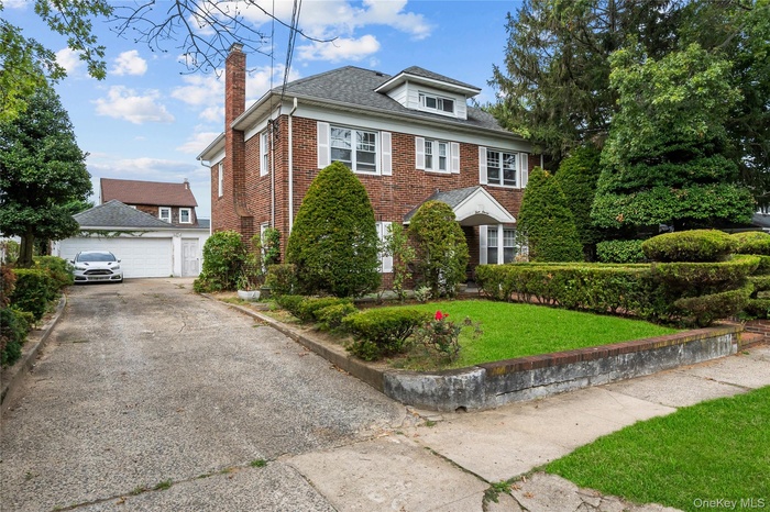 View of front facade featuring brick siding, a front lawn, a chimney, a shingled roof, and a detached garage