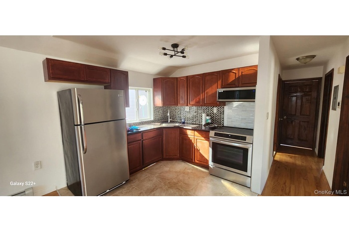 Kitchen with stainless steel appliances, decorative backsplash, dark countertops, light tile patterned flooring, and a baseboard radiator