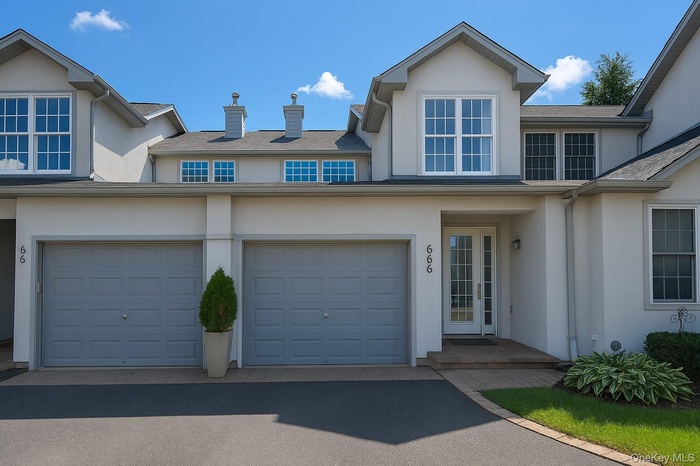 Traditional-style home with stucco siding, driveway, an attached garage, a chimney, and a shingled roof