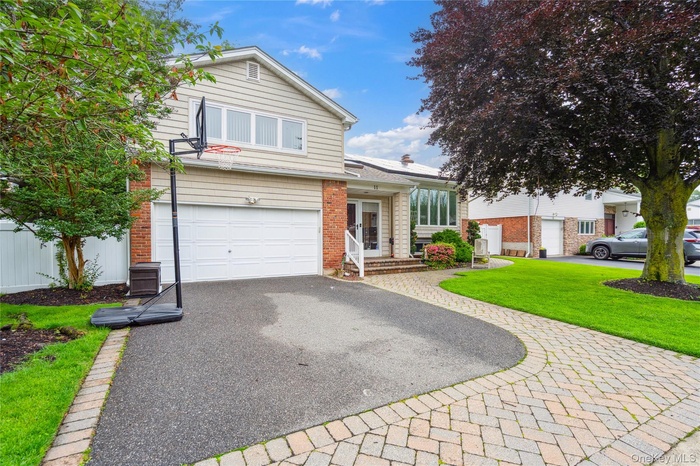 Traditional-style home with driveway, brick siding, a garage, and a front lawn