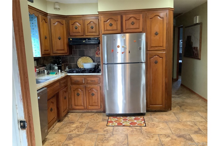 Kitchen featuring tasteful backsplash, stainless steel appliances, brown cabinetry, and under cabinet range hood
