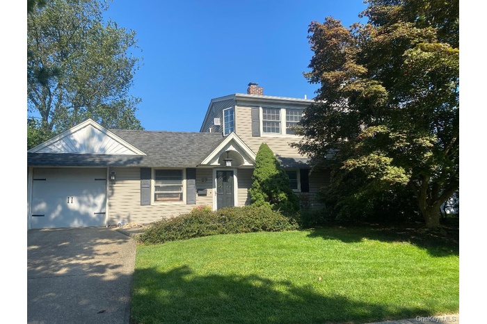 View of front facade featuring a front yard, a chimney, driveway, an attached garage, and a shingled roof