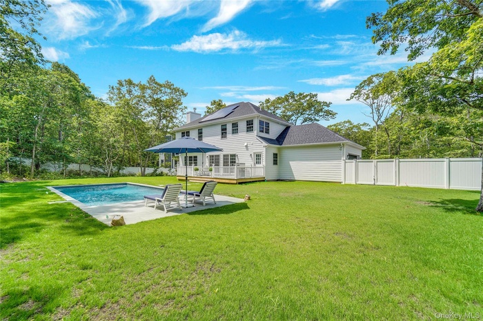 Rear view of house featuring a wooden deck, a chimney, a fenced backyard, and a patio area