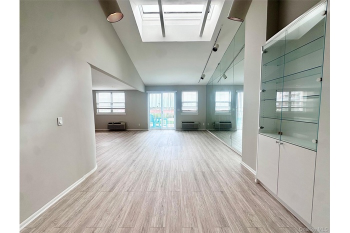 Unfurnished living room featuring light wood-type flooring, a skylight, and high vaulted ceiling