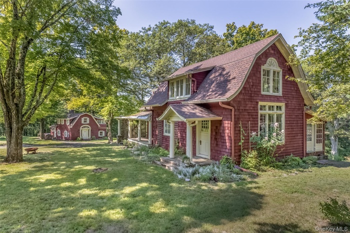 View of front of property with a shingled roof, a front lawn, view of wooded area, and a gambrel roof