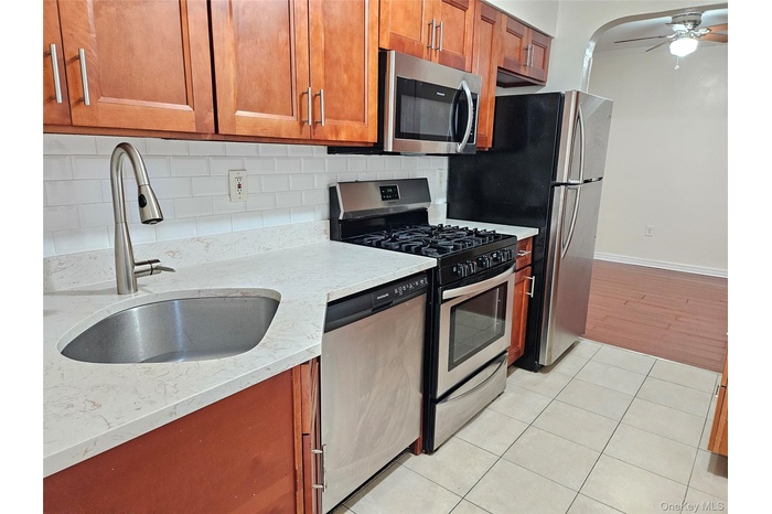 Kitchen with appliances with stainless steel finishes, tasteful backsplash, brown cabinets, light stone counters, and a ceiling fan