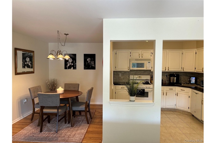 Kitchen with dark countertops, white appliances, backsplash, hanging light fixtures, and light wood-style floors