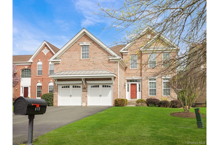 Traditional-style house with a standing seam roof, driveway, a front yard, brick siding, and an attached garage