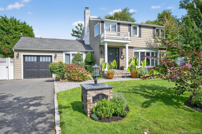 Colonial home with a garage, a front lawn, driveway, a chimney, and stone siding