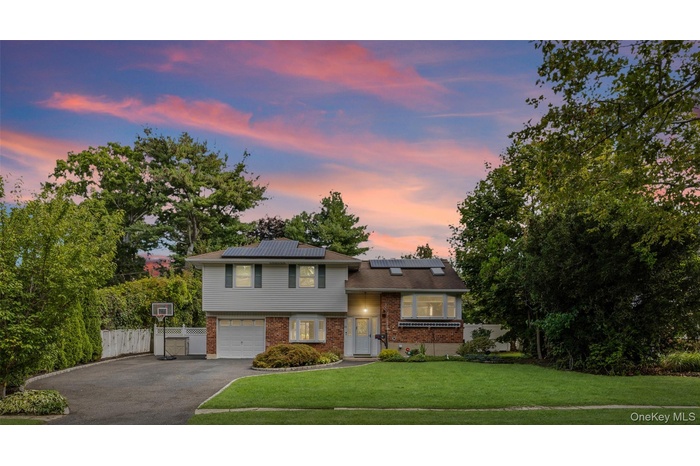 Tri-level home with driveway, brick siding, roof mounted solar panels, and an attached garage