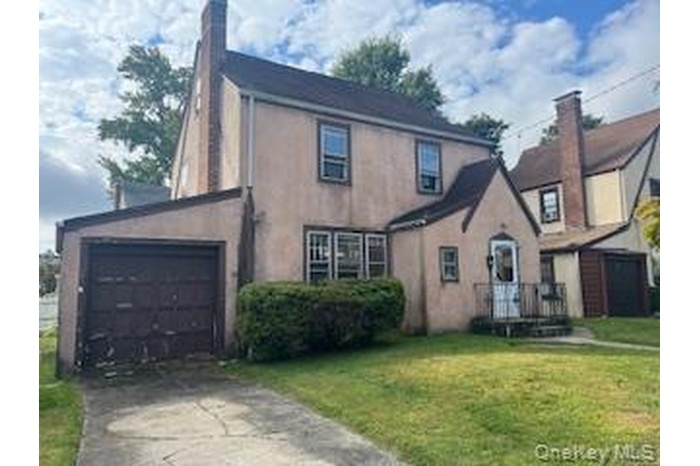 View of front facade with concrete driveway, a front lawn, a chimney, stucco siding, and an attached garage