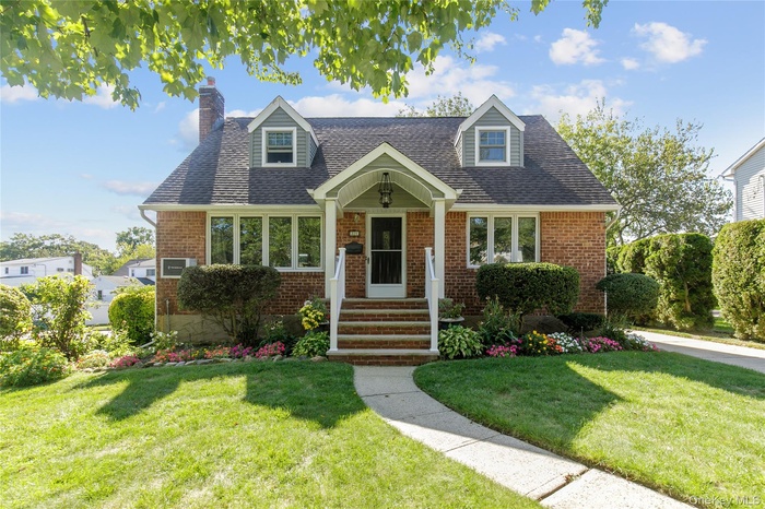 New england style home featuring brick siding, a front lawn, and a shingled roof